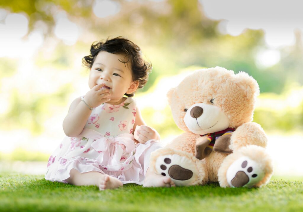 pexels photo 1166473 1166473 Smiling baby girl sits on grass with a plush teddy bear, enjoying a sunny day.